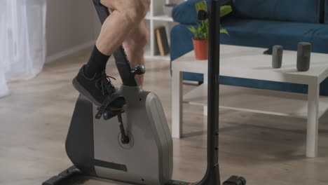 training-with-stationary-bicycle-at-home-closeup-view-of-legs-of-middle-aged-man-spinning-pedals-healthy-lifestyle-workout-indoors-with-equipment